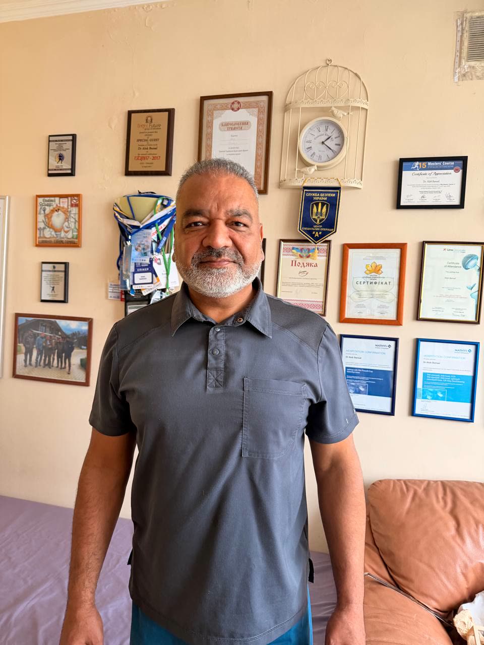 Dr. Alok Bansal біля стіни з дипломами, сертифікатами та подяками